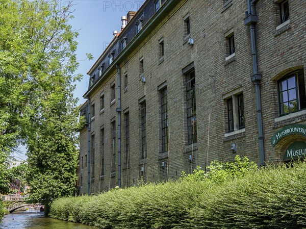 Large historic building along a canal in Bruges, surrounded by trees and green foliage, Bruges, Belgium, Europe