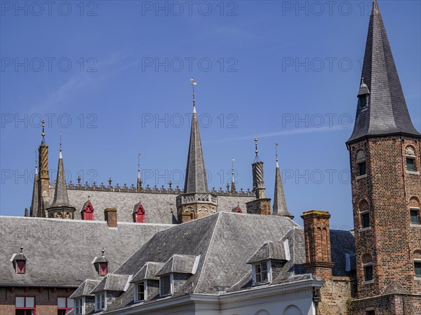 Historic building with many towers and battlements, grey roofs and bricks, under a blue sky, Bruges, Belgium, Europe