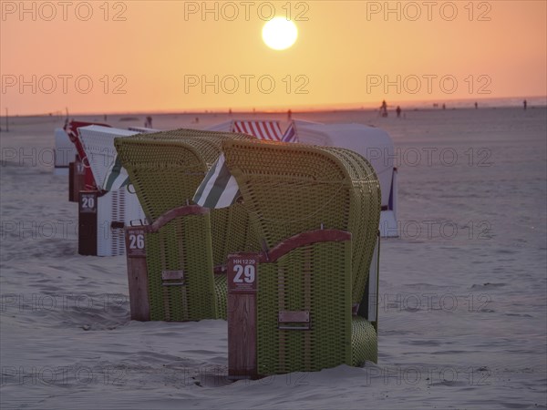 Beach chairs on the beach at sunset, the sky shining in warm orange tones, the sea in the background, juist, east frisia, germany