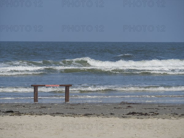 Sea beach with waves and empty bench in the foreground under a bright blue sky, Juist, East Frisia, Germany, Europe