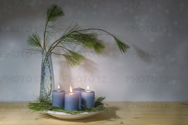 Blue candles, three lit for the third advent, and a vase with pine branches, modern decoration in the Christmas season, copy space, selected focus, narrow depth of field