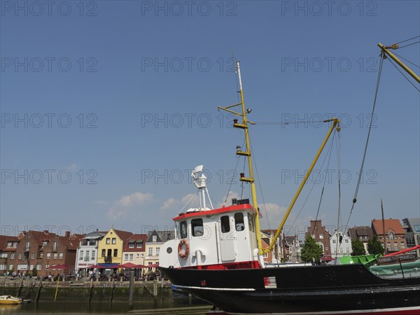 A harbour with a large boat in the foreground and colourful houses in the background under a blue sky, husum, schleswig-holstein, germany