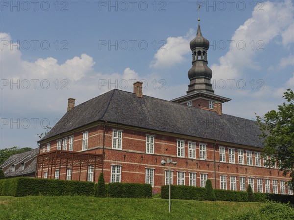 Large historic brick building with tower and windows on a green meadow under a blue sky, husum, schleswig-holstein, germany