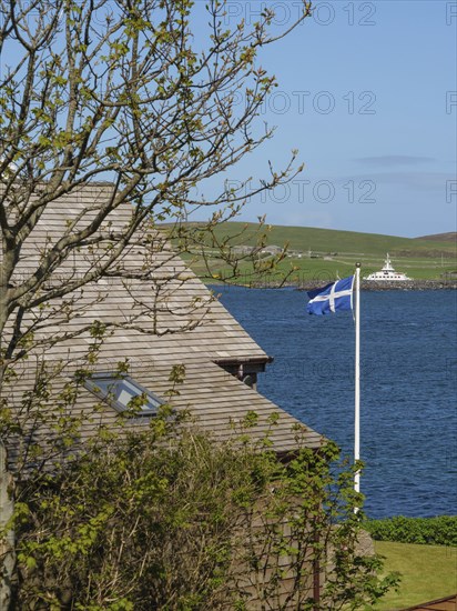 View of a coastal landscape with a house roof, a tree and a Scottish flag, Lerwick, Shetlands, Scotland, United Kingdom, Europe