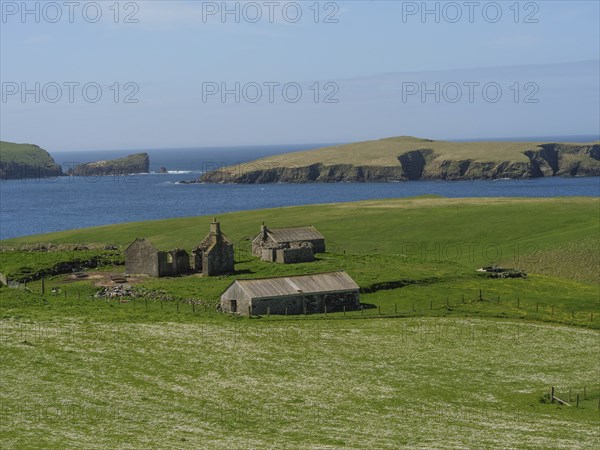 Green fields and old buildings in front of a coastline and islands in the sea, Lerwick, Shetlands, Scotland, United Kingdom, Europe