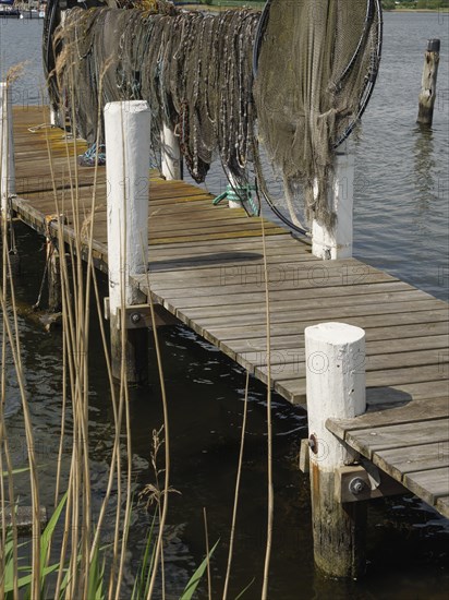 A wooden footbridge with suspended fishing nets leading into the water, Arnis, Schleswig-Holstein, Germany, Europe