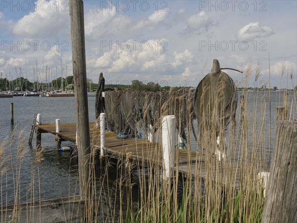 An old jetty on the lake with folded fishing nets, boats and clouds in the sky in the background, Arnis, Schleswig-Holstein, Germany, Europe