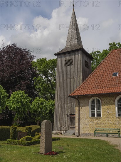 Historic wooden tower next to a sand-coloured church, surrounded by lush greenery, Arnis, Schleswig-Holstein, Germany, Europe