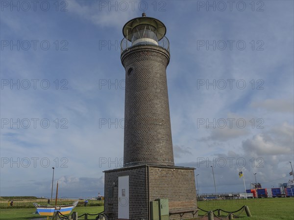 A tall brick lighthouse in a meadow with a few boats and a cloudy sky in the background, juist, east frisia, germany