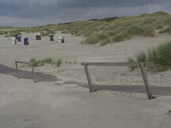 Deserted beach with a wooden path and scattered beach chairs under a cloudy sky, juist, east frisia, germany