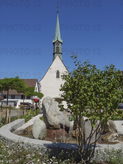 Church tower and fountain in a village surrounded by green trees and flowering plants on a sunny day, Meersburg, Lake Constance, Germany, Europe