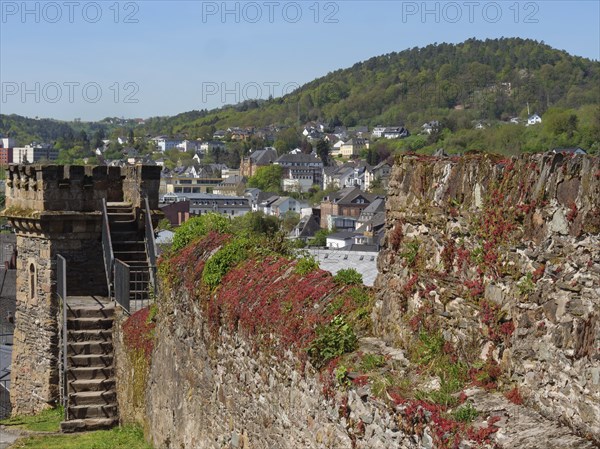 Historic tower and castle wall overlooking a green, hilly urban landscape on a sunny day, Saarburg, Germany, Europe
