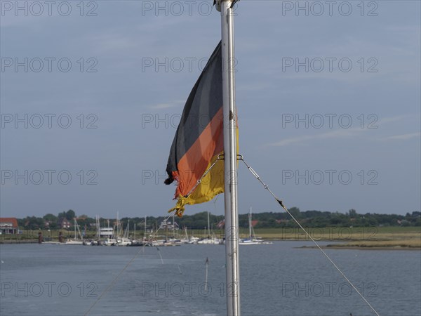 A German flag on a boat, surrounded by water and a quiet harbour, Spiekeroog, East Frisia, GERMANY