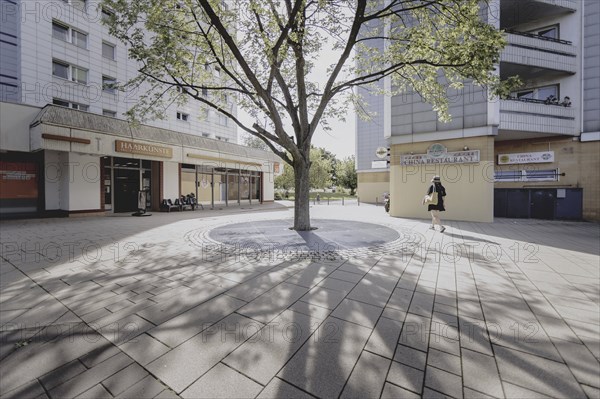 A woman walks next to a tree along a prefabricated building, taken in Berlin, 07/08/2024