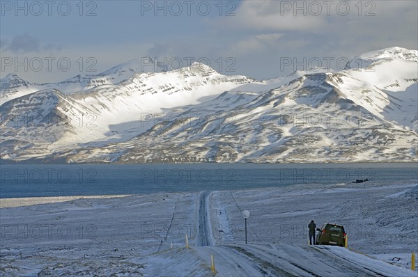 Snowy road leading to a lake, surrounded by mountains, with a car on the edge of the winter landscape, Skagarfjördur, North Iceland, Iceland, Europe
