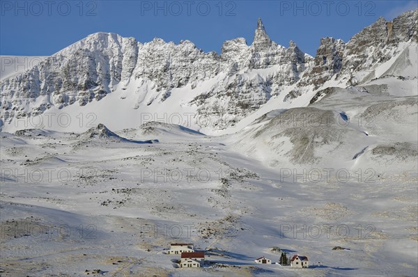Snow-covered mountains with small houses in the foreground under a clear blue sky, winter, Öxnadalur, Akureyri, Iceland, Europe