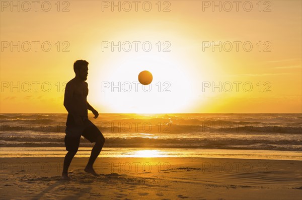 Great concept of soccer, man playing soccer on the beach in golden hour, sunset. Making keepie uppie