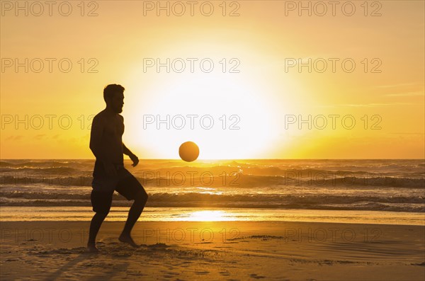 Great concept of soccer, man playing soccer on the beach in golden hour, sunset. Making keepie uppie