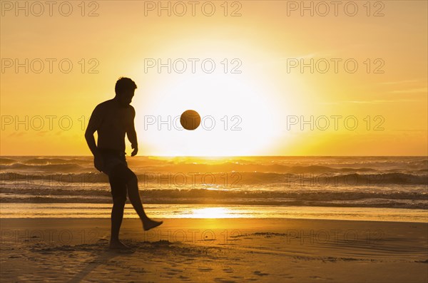 Great concept of soccer, man playing soccer on the beach in golden hour, sunset. Making keepie uppie