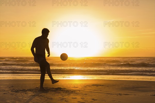 Great concept of soccer, man playing soccer on the beach in golden hour, sunset. Making keepie uppie