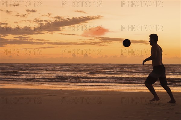 Great concept of soccer, man playing soccer on the beach in golden hour, sunset. Making keepie uppie