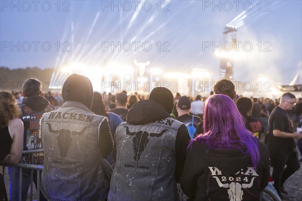Festival visitors with Wacken jackets look at the two main stages Faster and Harder at dusk at the Wacken Open Air in Wacken. The traditional metal festival takes place from 31 July to 3 August 2024