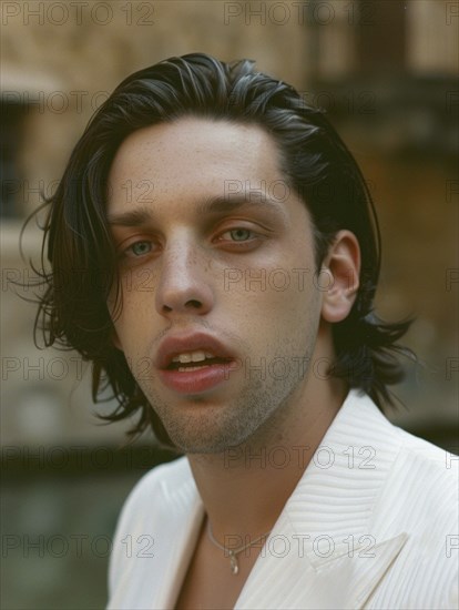 A close-up of a young man in a white jacket, looking introspective with natural light highlighting his features, AI generated