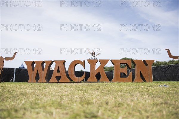 Festival visitor Hanna sits on the Wacken lettering at the Wacken Open Air in Wacken. The traditional metal festival takes place from 31 July to 2 August 2024
