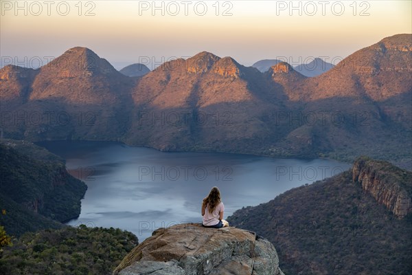 Young woman sitting on a rock, enjoying the view, sunset at Blyde River Canyon, view of canyon with Blyde River and table mountains in the evening light, canyon landscape, Panorama Route, Mpumalanga, South Africa, Africa