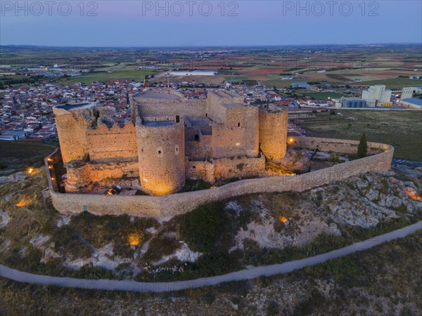 An old castle illuminated at night with a town and wide fields in the background at sunset, aerial view, Consuegra, Toledo, Castilla-La Mancha, Spain, Europe