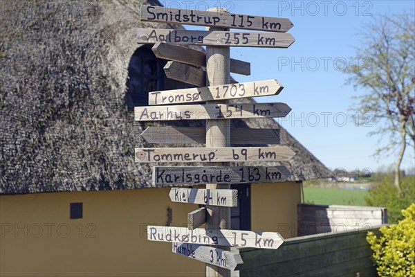A wooden signpost indicates various distances, next to a house with a thatched roof, Langeland, Denmark, Europe