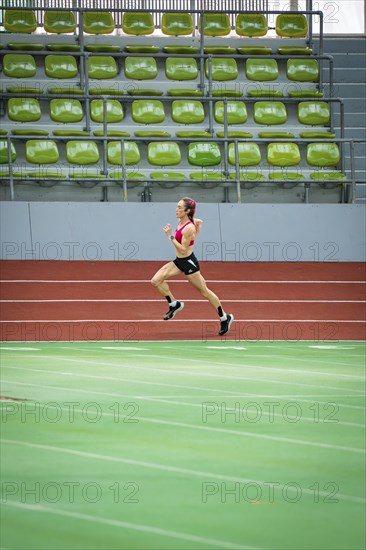 Lone runner trains on the running track of an empty stadium with green rows of seats, Glaspalast, Sindelfingen