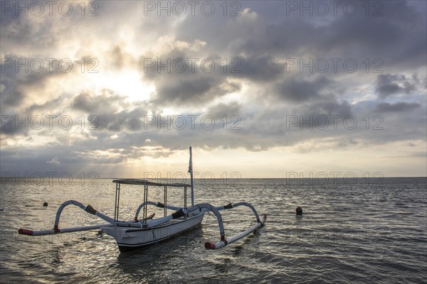 Jukung in the sea, typical landscape shot with a view of the horizon over the water, taken from a sandy beach. Traditional fishing boat at sunrise. Landscape shot of Sanur, Bali, Indonesia, Asia