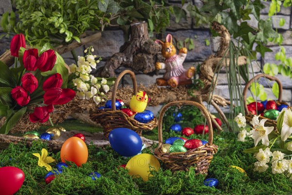 Easter basket with colourful eggs next to spring flowers and an Easter bunny on a moss-covered surface