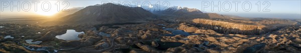 Panorama, White glaciated and snow-covered mountain peak Pik Lenin at sunrise, hilly landscape with golden meadows and lakes, aerial view, Trans Alay Mountains, Pamir Mountains, Osh Province, Kyrgyzstan, Asia