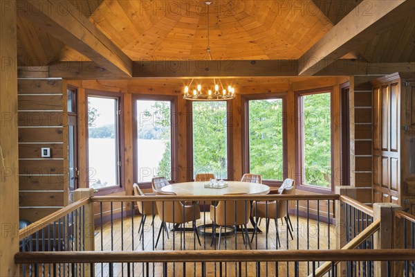 Staircase and round wooden dining table with tan leather armchairs in dining room inside a milled Eastern white pine timber and flat log profile home, Quebec, Canada. This image is property released. CUPR0362