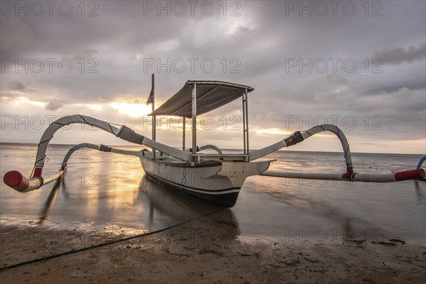 Jukung in the sea, typical landscape shot with a view of the horizon over the water, taken from a sandy beach. Traditional fishing boat at sunrise. Landscape shot of Sanur, Bali, Indonesia, Asia