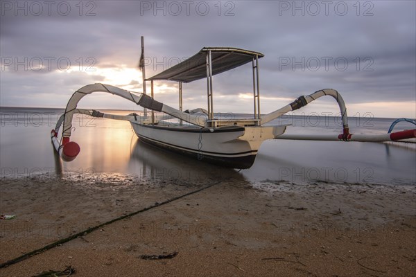 Jukung in the sea, typical landscape shot with a view of the horizon over the water, taken from a sandy beach. Traditional fishing boat at sunrise. Landscape shot of Sanur, Bali, Indonesia, Asia