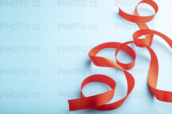 Red coral ribbon on a blue pastel background. Celebration concept. Side view, copy space