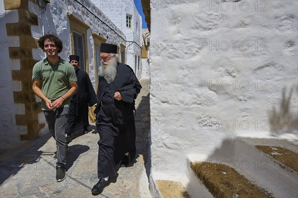 Course between a priest in black clothes and a younger man, narrow white alley, sunny atmosphere, Chora, main town Patmos, Patmos, Old Town, Dodecanese, Greek Islands, Greece, Europe