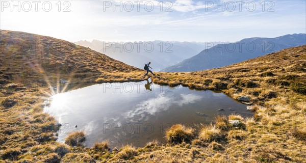 Mountaineer jumping, reflected in a small mountain lake on the Krahberg, mountain panorama in autumn, Venet crossing, Ötztal Alps, Tyrol, Austria, Europe