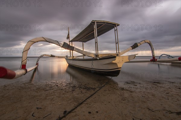 Jukung in the sea, typical landscape shot with a view of the horizon over the water, taken from a sandy beach. Traditional fishing boat at sunrise. Landscape shot of Sanur, Bali, Indonesia, Asia
