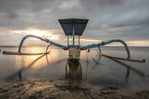 Jukung in the sea, typical landscape shot with a view of the horizon over the water, taken from a sandy beach. Traditional fishing boat at sunrise. Landscape shot of Sanur, Bali, Indonesia, Asia