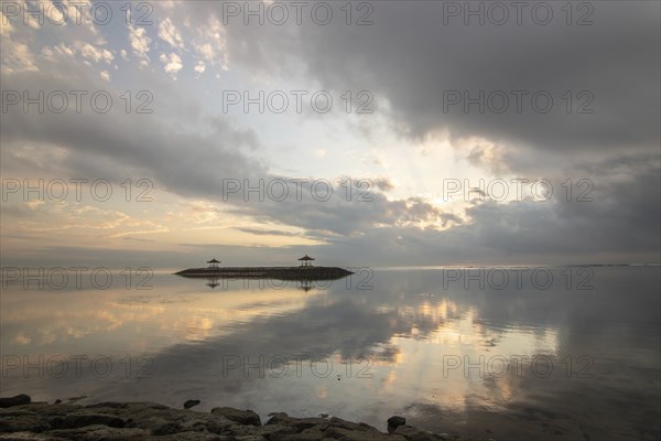 Beautiful seascape in the morning. Tropical sandy beach with breakwater and reflection of the sky in the calm water. Morning landscape, taken in Sanur, Bali, Indonesia, Asia