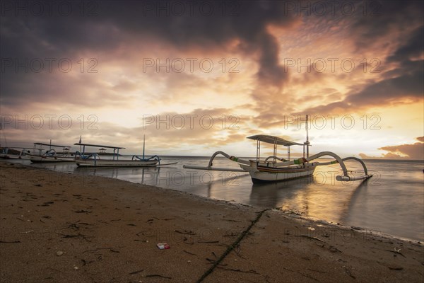 Jukung in the sea, typical landscape shot with a view of the horizon over the water, taken from a sandy beach. Traditional fishing boat at sunrise. Landscape shot of Sanur, Bali, Indonesia, Asia