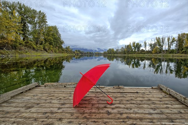 A concept photo of a red umbrella resting on a wooden dock by Kootenai RIver in north Idaho during autumn