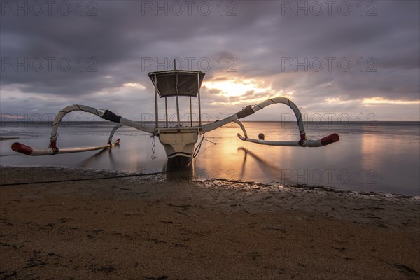 Jukung in the sea, typical landscape shot with a view of the horizon over the water, taken from a sandy beach. Traditional fishing boat at sunrise. Landscape shot of Sanur, Bali, Indonesia, Asia