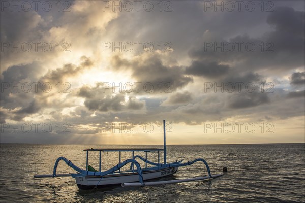 Jukung in the sea, typical landscape shot with a view of the horizon over the water, taken from a sandy beach. Traditional fishing boat at sunrise. Landscape shot of Sanur, Bali, Indonesia, Asia