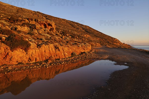A road next to a reflecting puddle of water at sunrise lighting in a rocky landscape, Gramvoussa peninsula, north-west Crete, Crete, Greek Islands, Greece, Europe