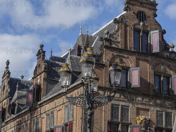 Historic brick building with ornate windows and decorative lanterns under a cloudy sky, nijmegen, the netherlands